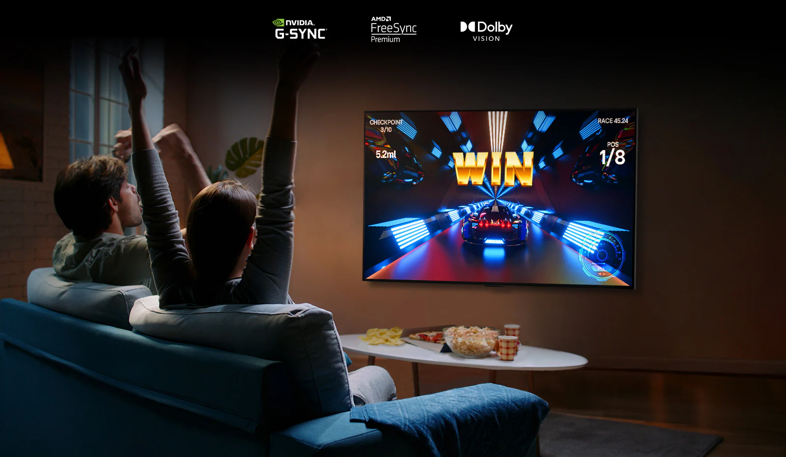 Two people sit on a couch playing a racing game with a controller and LG OLED G2 in a living room.